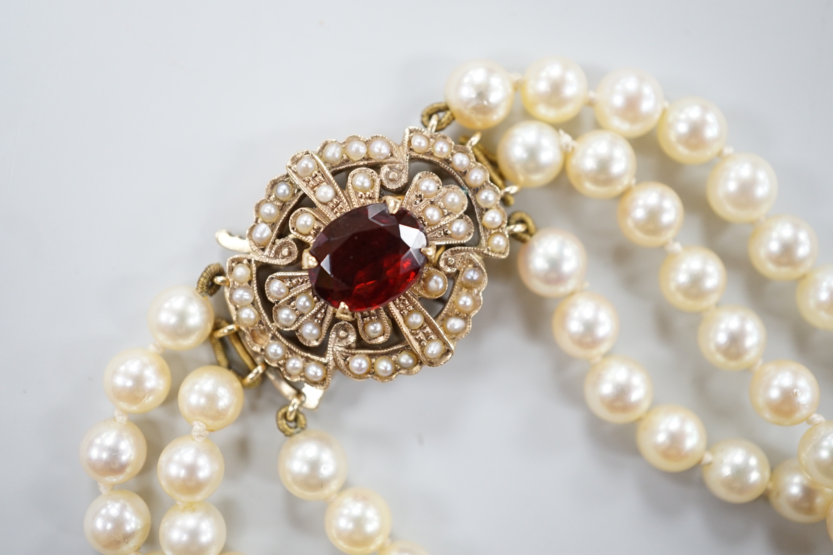 A 1960's triple strand cultured pearl choker necklace by Cropp & Farr, with 9ct gold, garnet and seed pearl set clasp, 39cm.